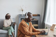 © Seventyfour - Portrait of contemporary couple using internet devices at home, focus on African-American man wearing headphones at desk in foreground, copy space