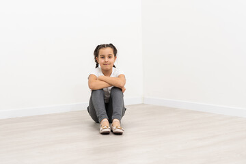 Wall Mural - Smiling little girl in full length sitting over white background and looking up