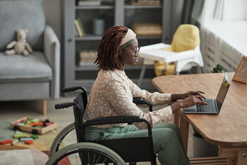 Wall Mural - High angle portrait of young African-American woman using wheelchair while working from home with childrens toys in background, copy space