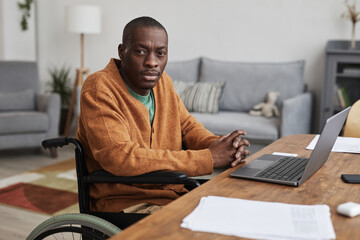 Wall Mural - Portrait of adult African-American man using wheelchair while working from home and looking at camera, copy space