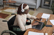 © Seventyfour - High angle portrait of African-American woman in wheelchair online shopping via laptop and holding credit card, copy space