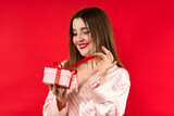 Fototapeta Na ścianę - Portrait of a happy young woman holding present box isolated over red background