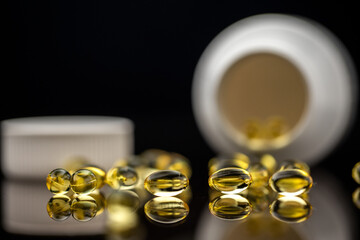 Yellow vitamin D capsules with reflection. Pharmaceutical medicament. Pills, tablets, drug, vitamin, capsules isolated on black background. Medicine and healthcare.