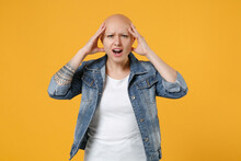Young Bald Caucasian Shocked Surprised Troubled Woman 20s Without Hair Wearing Casual Denim Jacket White T-shirt Open Mouth Looking Camera Hold Head Isolated On Yellow Background Studio Portrait.