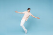 © ViDi Studio - Full length of young caucasian attractive smiling student man 20s in beige t-shirt white pants leaning over with outstretched hands looking aside isolated on blue color background studio portrait