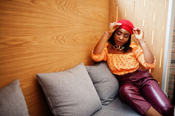 Wall Mural - Elegant afro american woman in red french beret, big gold neck chain polka dot blouse and leather pants pose indoor.