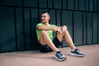 © BullRun - Caucasian male sportsman with modern cellphone device in hand looking away while resting at urbanity, muscular runner in active wear using smartphone during morning time for physical training