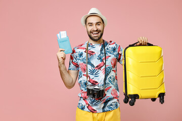 Canvas Print - Cheerful young traveler tourist man in summer clothes hat photo camera hold suitcase passport ticket looking aside isolated on pink background. Passenger travel on weekend. Air flight journey concept.