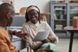© Seventyfour - Portrait of modern African-American couple working from home together, focus on smiling young woman holding document while sitting on floor, copy space