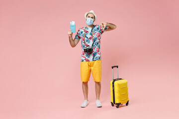 Wall Mural - Full length displeased traveler tourist man in mask safe from coronavirus hold passport tickets showing thumb down isolated on pink background. Passenger travel on weekend. Air flight journey concept.