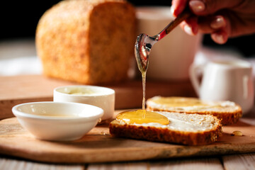 Side view on spreading bread slice with honey on the wooden cutting board