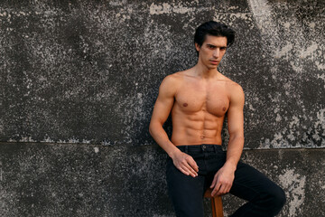 Wall Mural - Outside portrait of a hot fit young man with muscular body and bare torso showing six pack abs posing at old black wall.