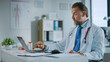 © Gorodenkoff - Happy Family Medical Doctor is Working on a Laptop Computer in a Health Clinic. Physician in White Lab Coat is Browsing Medical History Behind a Desk in Hospital Office.