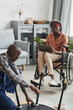 © Seventyfour - Vertical portrait of young African-American woman in wheelchair watching handyman assembling furniture, online service and assistance concept