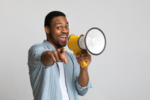 Positive African Guy Shouting In Megaphone Over Grey Background