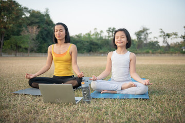 Wall Mural - Mother and daughter doing yoga. woman and child training in the park. outdoor sports. healthy sport lifestyle,watching yoga exercises online video tutorial and meditation practice during work out.