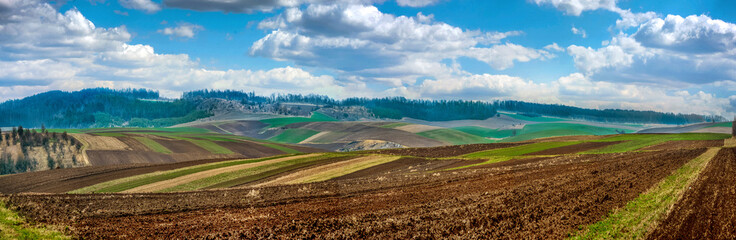 Fotomurales - spring wide panorama of arable fields stretching to horizon under bright blue sky with clouds on distant hills. Agriculture and farming concept.