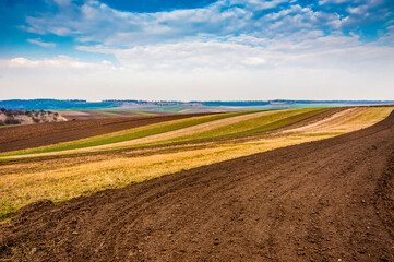 Fotomurales - spring field, plowed lands lines, relief hilly landscape in the background