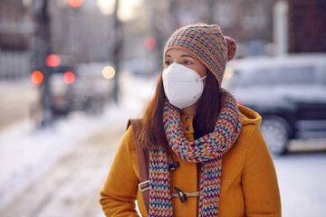 Middle-aged brunette woman in winter clothes wearing face mask outdoors due to Corona virus outdoors while on her way to work