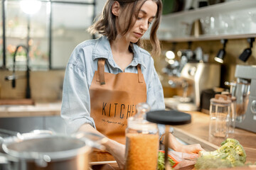 Wall Mural - Pretty housewife in kitchen apron cooking healthy food at beautiful interior. Healthy and wellness concept. High quality photo