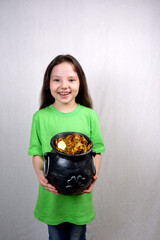 Charming seven years old girl laugh and showing off cast iron pot, decorated by clover leaf, full of leprechaun's gold. St. Patrick's Day holiday motif