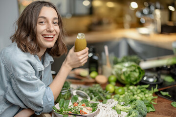 Wall Mural - Pretty young woman enjoy healthy clean food on the kitchen. Drinking a green smoothie with vegetable ingredients on the table. High quality photo