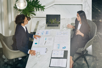 Wall Mural - Young serious business woman explaining her idea to colleague when they are having meeting and discussing charts and reports