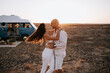 © Alejandro Diaz/ADDICTIVE STOCK - Side view of positive traveling couple in white clothes hugging and standing in savanna on background of sundown sky during summer vacation