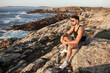 © Andres Victorero/ADDICTIVE STOCK - Side view of peaceful male sitting on rock on coast and admiring calm seascape at sundown in summer
