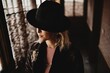 © Carlos Pintau/ADDICTIVE STOCK - Charming pensive young female in elegant vintage clothes and hat standing in front of window in dark room