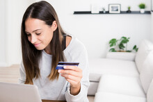 Female Buyer Sitting On Sofa At Home And Making Payment With Plastic Card While Shopping Online Via Laptop