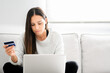 © Chris Leon/ADDICTIVE STOCK - Female buyer sitting on sofa at home and making payment with plastic card while shopping online via laptop