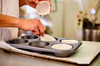 © Cien X Cien Studio/ADDICTIVE STOCK - Side view of crop anonymous confectioner arranging paper cups into metal muffin tray before filling with dough while preparing pastry in kitchen