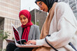 © David Munoz/ADDICTIVE STOCK - Content Arab female students in headscarf sitting on bench in green garden of campus and preparing for exams while reading notes and using laptop