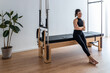 © David Fuentes/ADDICTIVE STOCK - Delighted athletic female in sportswear sitting on pilates cadillac reformer and relaxing during training in bright gym
