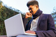 © David Munoz/ADDICTIVE STOCK - Low angle of African American male entrepreneur sitting on street with clenched fist and closed eyes while working on laptop and waiting for approval of project