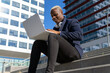 © David Munoz/ADDICTIVE STOCK - From below of content African American male entrepreneur in stylish wear sitting on stairs in city center and typing on laptop while working remotely on project
