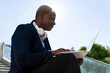© David Munoz/ADDICTIVE STOCK - Side view of content African American male entrepreneur in stylish wear sitting on stairs in city center and typing on laptop while working remotely on project
