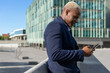 © David Munoz/ADDICTIVE STOCK - Side view of smiling African American businessman standing in downtown and messaging on smartphone while discussing project details online