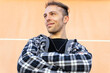 © David Munoz/ADDICTIVE STOCK - From below positive confident young hipster guy in casual checkered shirt looking away and smiling while standing against orange wall