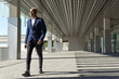 © David Munoz/ADDICTIVE STOCK - Cheerful black male entrepreneur in stylish formal outfit walking along sunny street and looking away