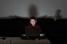 Surprised Excited Boy Sitting On Sofa In Dark Room And Watching Film On Laptop