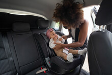 Caring African American Mother Tenderly Putting Cute Toddler In Modern Baby Car Seat