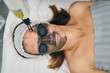 © Gabriel Trujillo/ADDICTIVE STOCK - From above anonymous cosmetician using machine for carbon peel on face of female client lying in protective glasses in beauty clinic