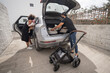 © Fran Rosado/ADDICTIVE STOCK - Back view of ethnic man putting luggage and baby stroller in trunk and African American mother with toddler getting in car while preparing for trip