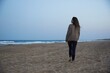 © German Linares/ADDICTIVE STOCK - Back view of barefoot woman in shawl standing on sandy coast against wavy ocean