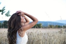 Side view calm slim brunette touching long hair sitting alone with eyes closed on meadow in countryside looking away in dreams