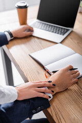 Wall Mural - cropped view of secretary touching hand of businessman near notebook and laptop, blurred background
