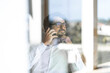 © Joao - Man wearing glasses making a cell phone call sitting down looking through the window. Successful male portrait working from home