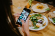 © Jake Jakab/ADDICTIVE STOCK - From above cropped unrecognizable female at table taking photo of food on smartphone for social media